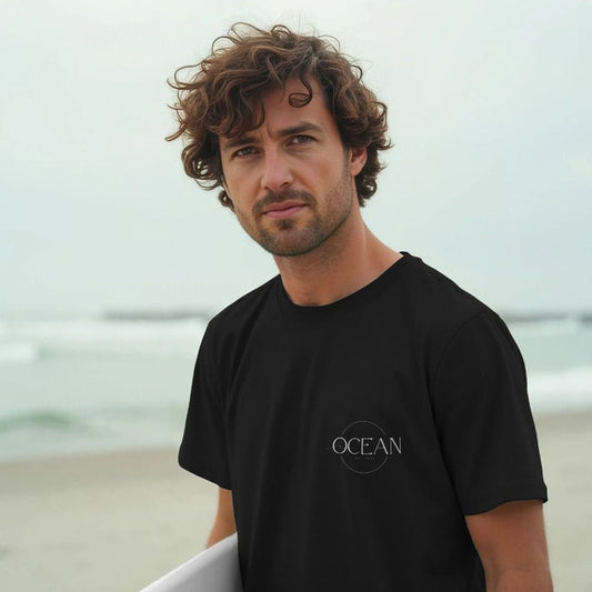 Man wearing a black t-shirt with 'OCEAN' logo on a beach